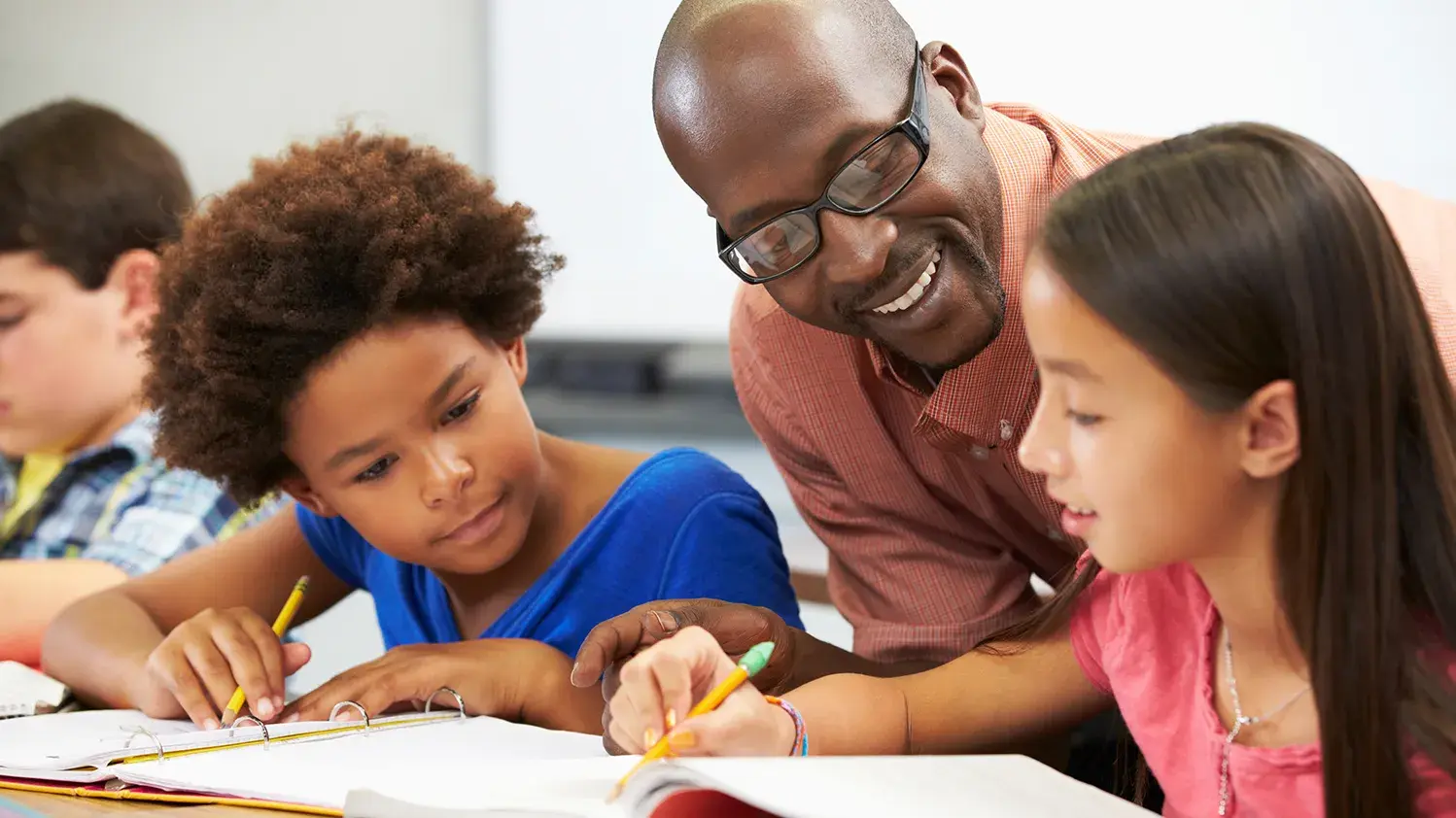 A teacher stands helping two students with homework
