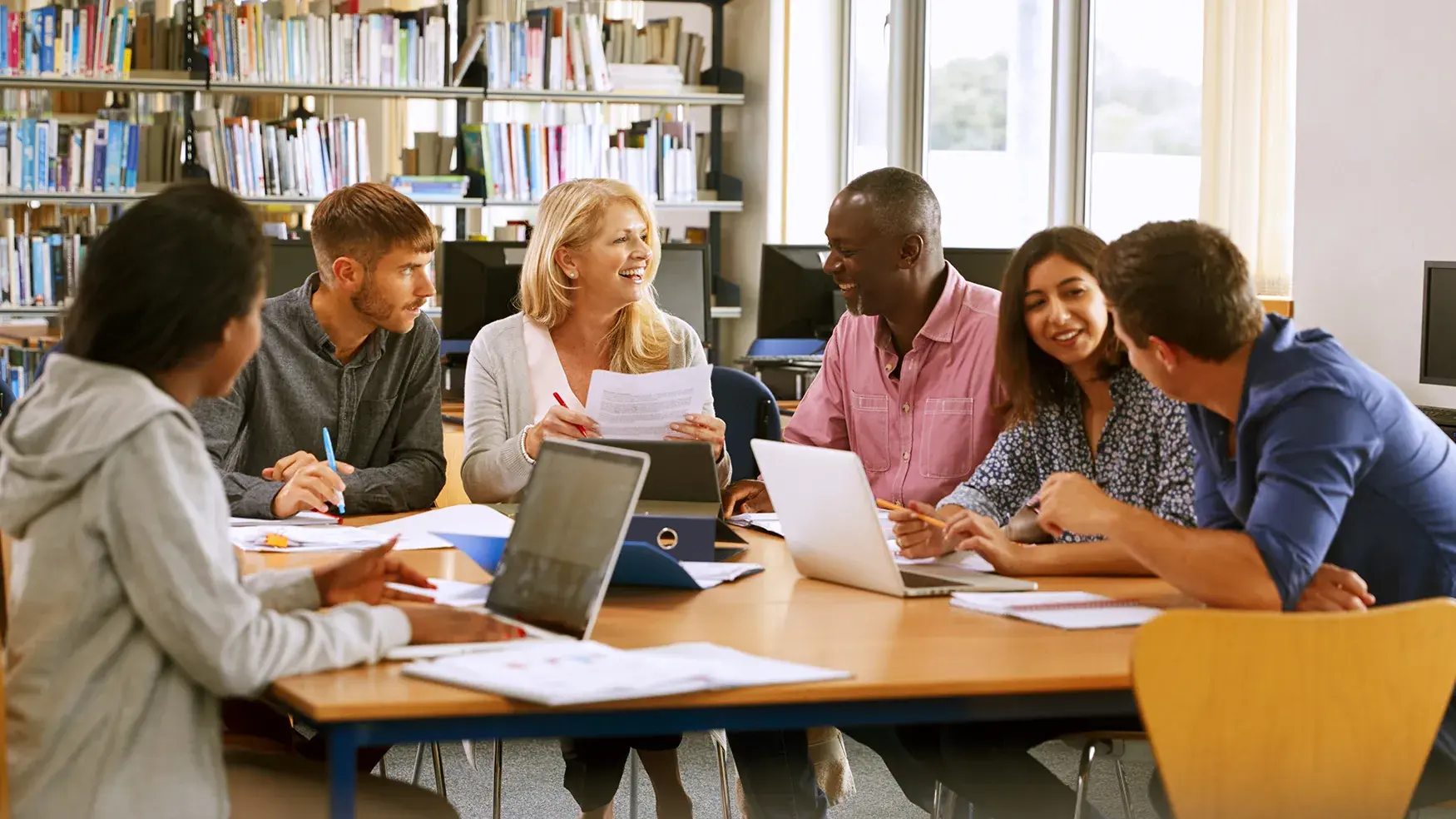small group of young adults workshop around a large table in a library setting