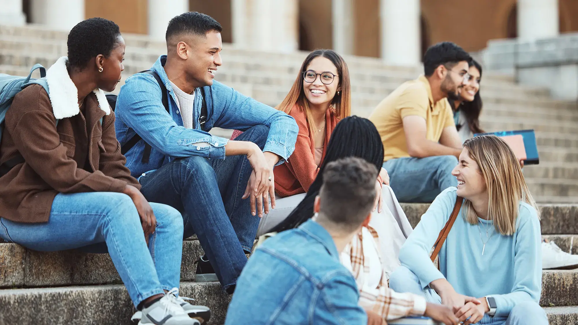 students laugh in a group while sitting on the steps of a college campus