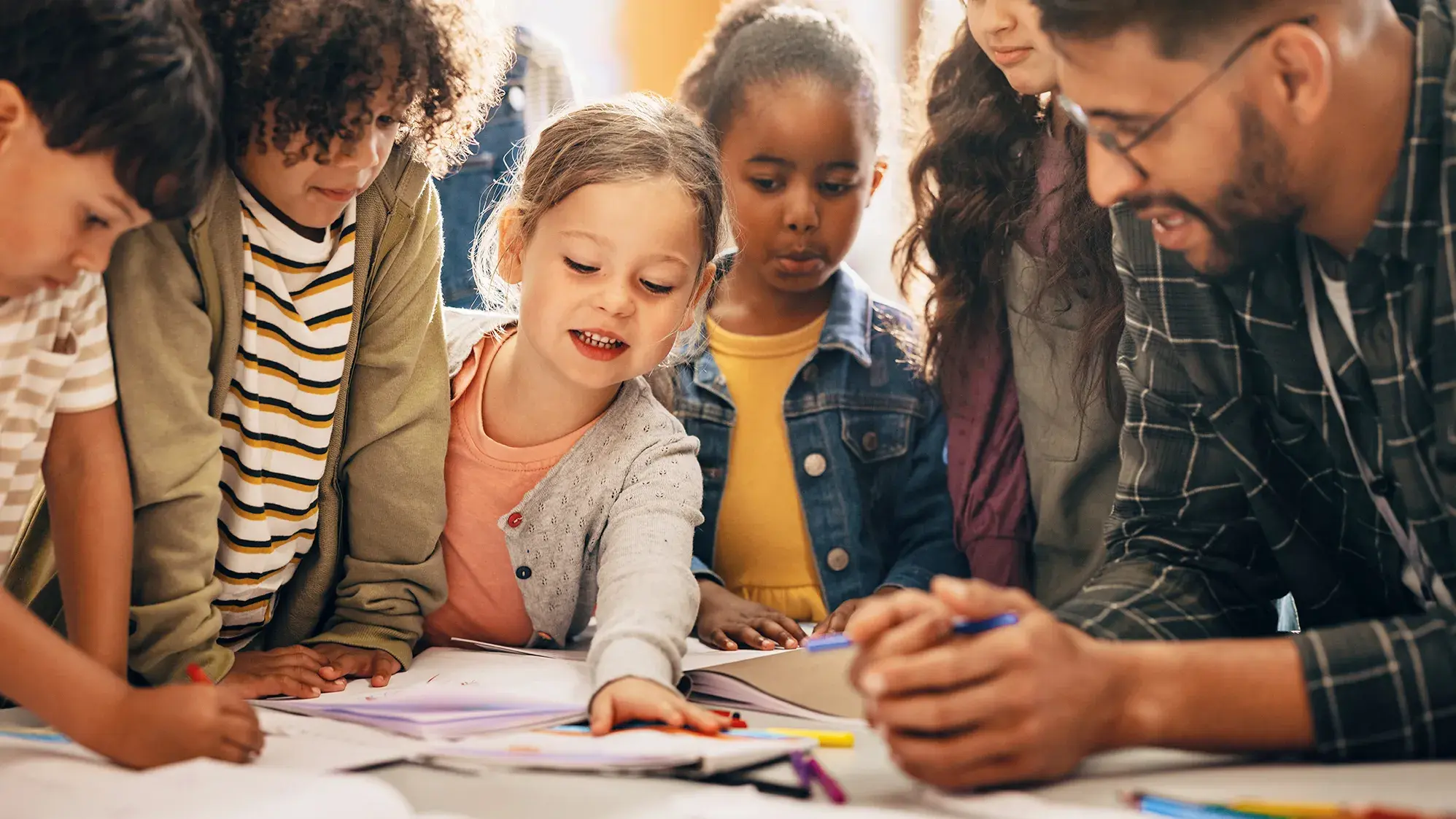 small group of children looking at workbook materials in a classroom with their teacher